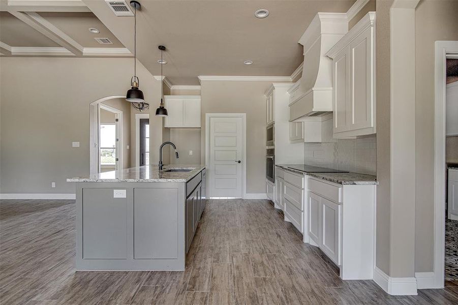 Kitchen featuring sink, stainless steel appliances, white cabinets, decorative light fixtures, and a center island with sink