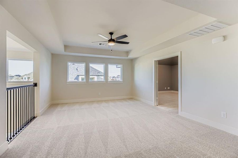 Empty room with a tray ceiling, light carpet, and ceiling fan