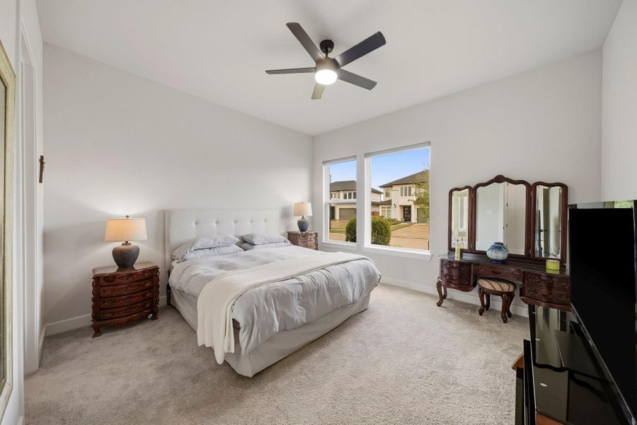 This downstairs secondary bedroom offers comfort and privacy with plush carpet, an 8-foot interior door, and a ceiling fan with integrated light. Roller shades dress the windows, providing convenient light control while completing the room’s clean, upscale presentation.