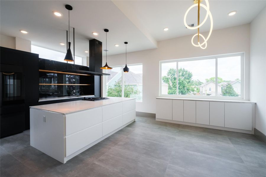 Representative Middle Level Kitchen View (Design selections and colors may vary): This exquisite space on the middle level features a backdrop of matted black cabinets with floating shelves, playfully shaped pendant lights, and white cabinets that seamlessly extending the 9-foot white quartz island. This kitchen combines form and function with sleek touches such as a gas rangetop with griddle (built-in microwave and dishwasher not pictured), a Italian range hood, and a multi-function sink.