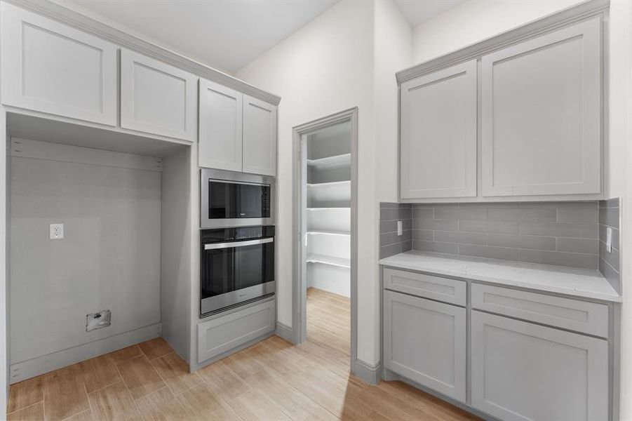 Kitchen featuring appliances with stainless steel finishes, light wood-style floors, light stone counters, and decorative backsplash