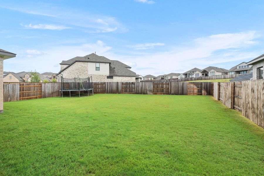 A spacious backyard enclosed by a tall wooden fence provides privacy and room for outdoor activities.