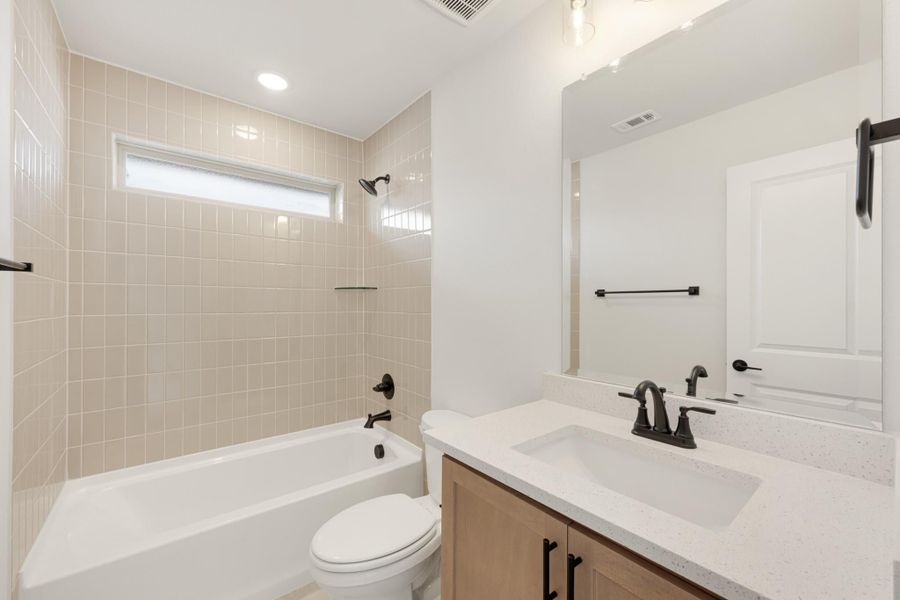 Bathroom with beige tiled tub surround, white quartz vanity, wood cabinets, and black fixtures
