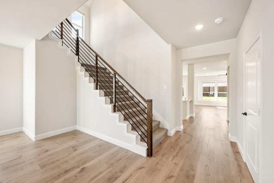 Entryway with carpeted staircase, metal railing, and light hardwood floors leading to main living area