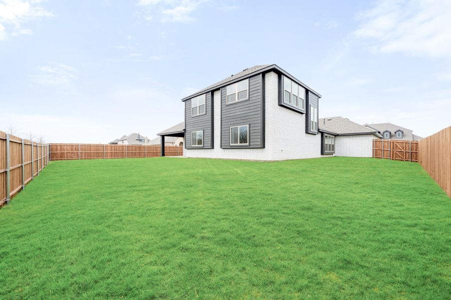 Backyard of two-story home with gray siding, large green lawn, and wood privacy fence