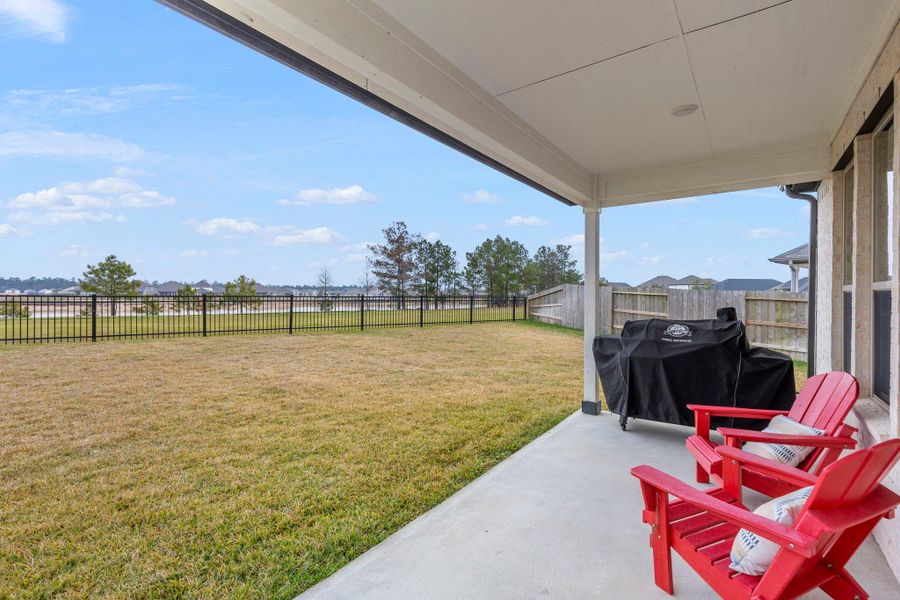 Spacious backyard with a covered patio featuring red Adirondack chairs and a grill. The area is fenced, offering a clear view of the surrounding landscape. Ideal for outdoor relaxation and entertaining. Spacious backyard with a covered patio featuring red Adirondack chairs and a grill. The area is fenced, offering a clear view of the surrounding landscape. Ideal for outdoor relaxation and entertaining.