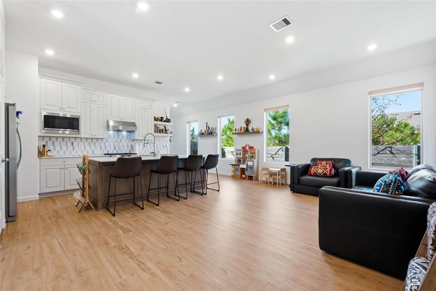 This spacious open-concept living area features a modern kitchen with white cabinetry and stainless steel appliances, a large island with seating, and a cozy living space with ample natural light from multiple windows