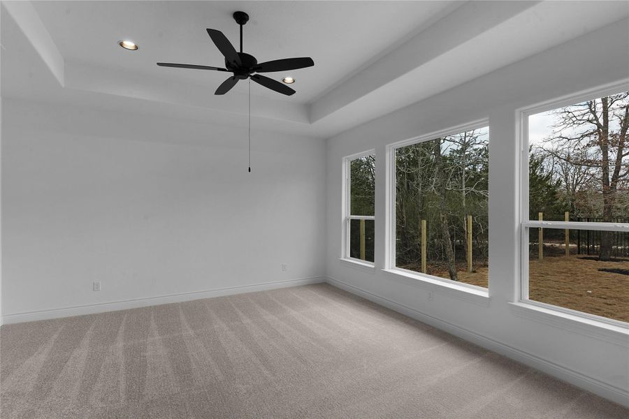 Empty room with a raised ceiling, ceiling fan, light carpet, and recessed lighting