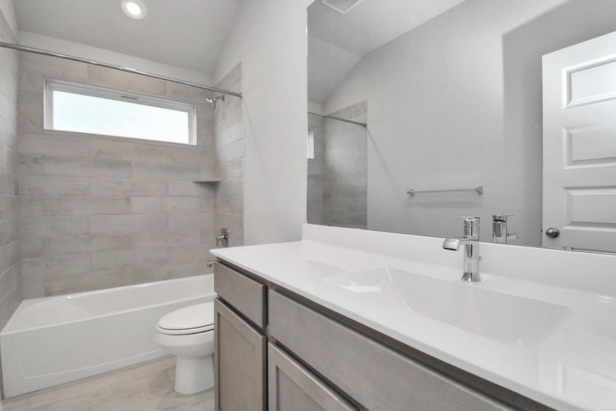 Secondary bath features tile flooring, bath/shower combo with tile surround, light stained wood cabinets, beautiful light countertop.
