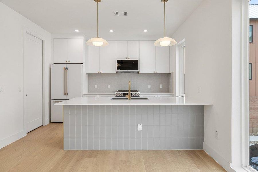Kitchen with a peninsula, white cabinetry, white appliances, light wood-type flooring, and backsplash