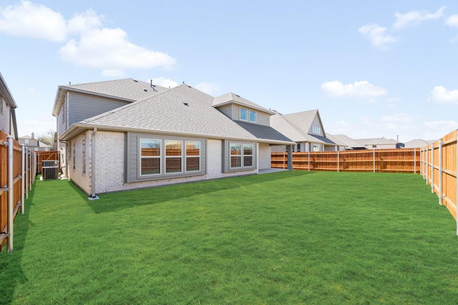 Backyard of brick home with large green lawn and wood privacy fence on both sides