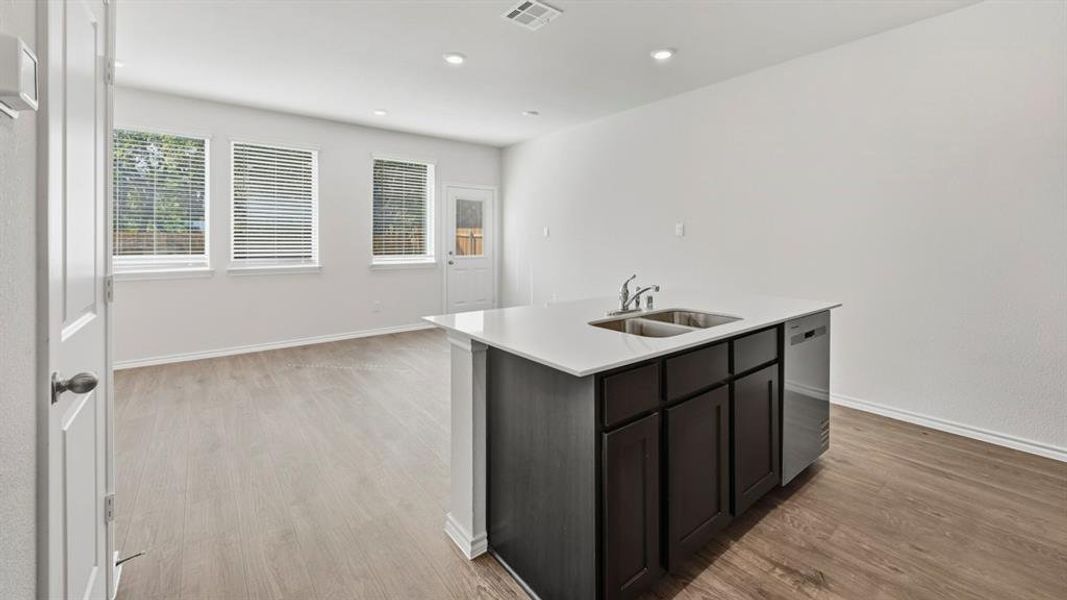 Kitchen with an island with sink, stainless steel dishwasher, light wood-style floors, recessed lighting, and light stone countertops