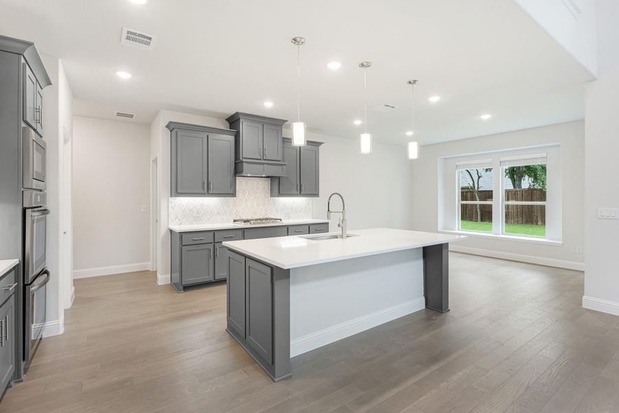 Open kitchen with gray cabinets, large center island with sink, pendant lights, and hardwood floors Open kitchen with gray cabinets, large center island with sink, pendant lights, and hardwood floors