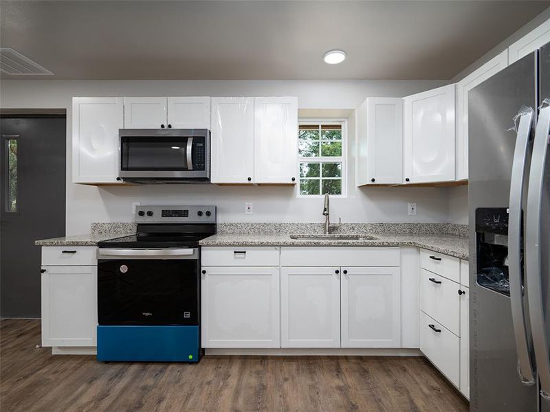 Kitchen featuring appliances with stainless steel finishes, white cabinets, dark wood finished floors, and light stone counters