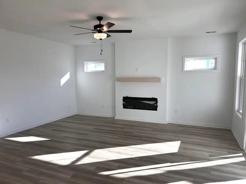 Unfurnished living room with a glass covered fireplace, dark wood finished floors, and a ceiling fan