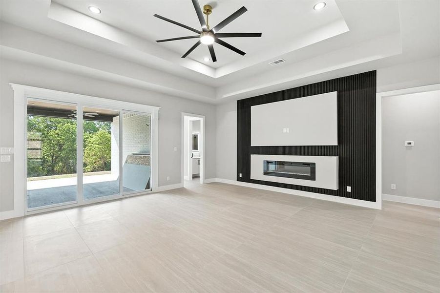Unfurnished living room featuring a glass covered fireplace, a tray ceiling, a ceiling fan, and recessed lighting Unfurnished living room featuring a glass covered fireplace, a tray ceiling, a ceiling fan, and recessed lighting