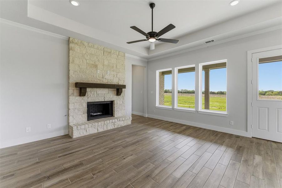 Unfurnished living room with a ceiling fan, wood finish floors, a fireplace, and a raised ceiling