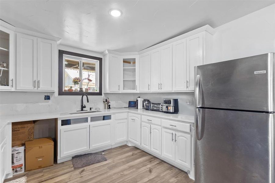 Kitchen featuring freestanding refrigerator, glass insert cabinets, white cabinets, and light wood-style floors Kitchen featuring freestanding refrigerator, glass insert cabinets, white cabinets, and light wood-style floors