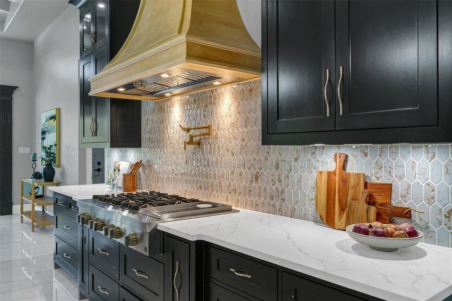 Kitchen with premium range hood, stainless steel gas cooktop, light stone countertops, and tasteful backsplash