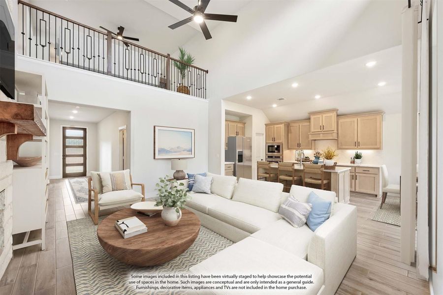 Open-concept living room with two-story ceiling, ceiling fan, white sectional sofa, and kitchen visible in background