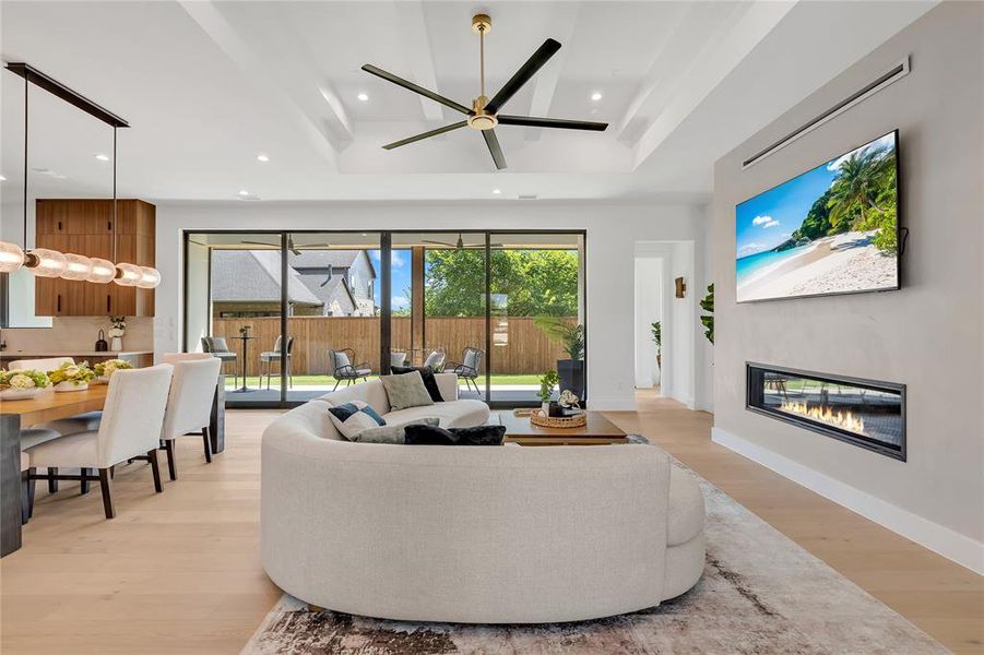 Living room featuring light wood-type flooring, a glass covered fireplace, recessed lighting, a ceiling fan, and a tray ceiling Living room featuring light wood-type flooring, a glass covered fireplace, recessed lighting, a ceiling fan, and a tray ceiling