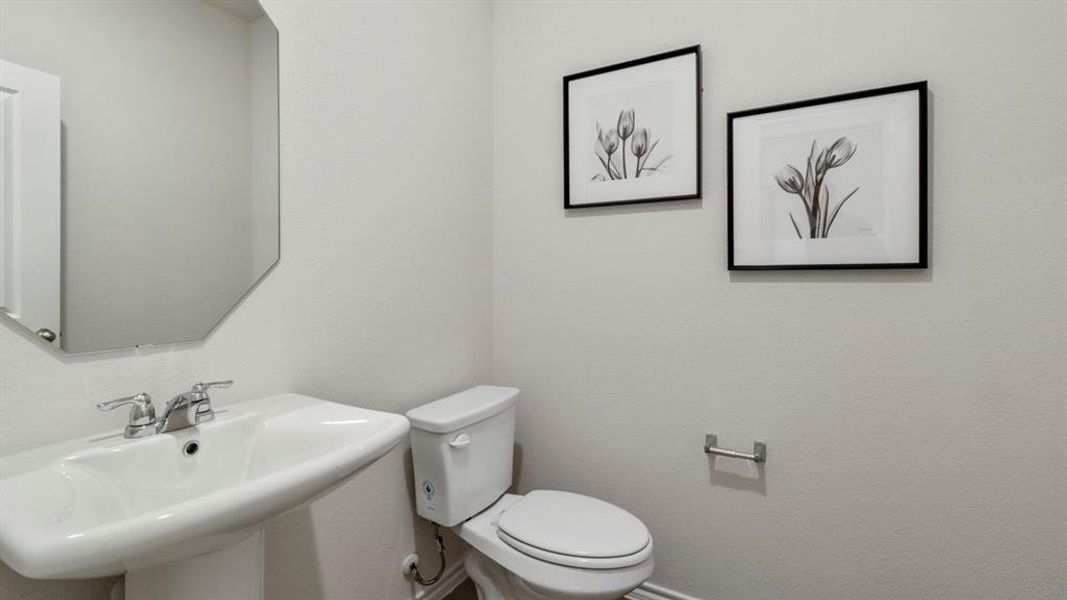 Pedestal sink with chrome faucet, an octagonal wall-mounted mirror, and a white toilet
