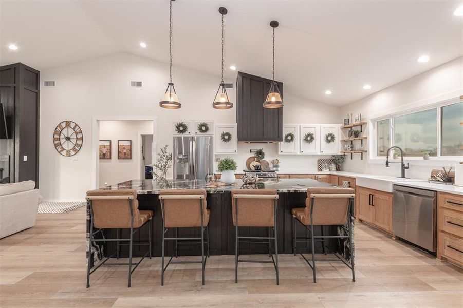 Kitchen featuring a breakfast bar area, stainless steel appliances, decorative light fixtures, a large island, and dark stone countertops