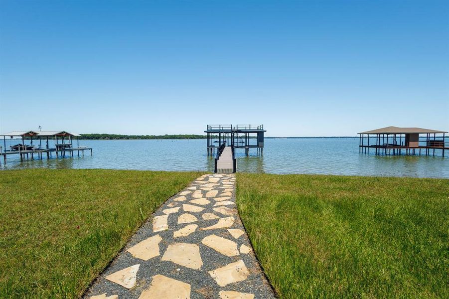 Stone-paved pathway leading to a multi-level boat dock with a covered slip and upper deck