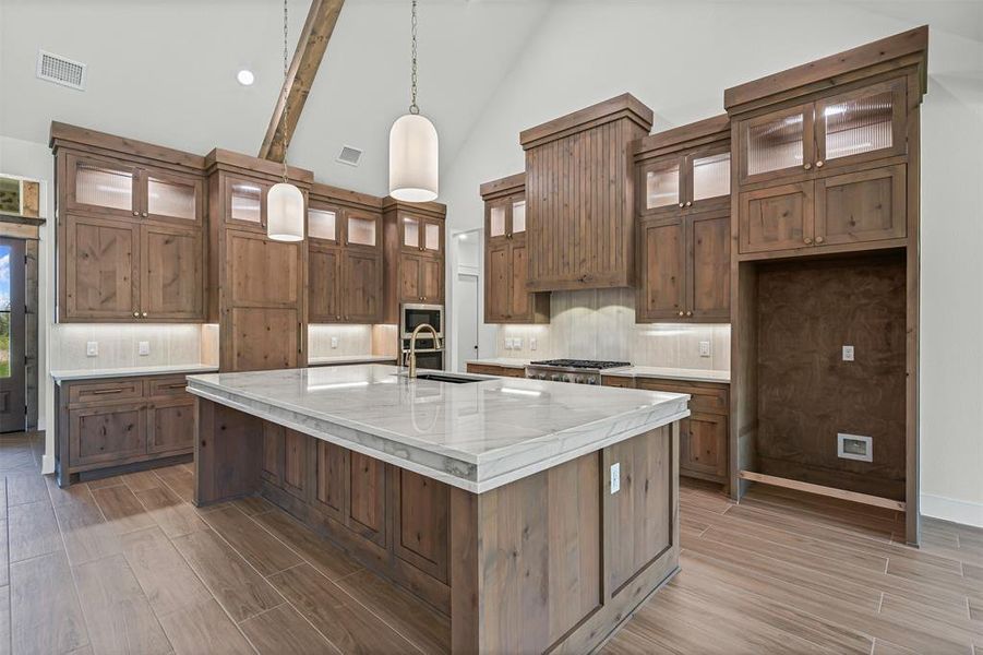 Kitchen with decorative backsplash, high vaulted ceiling, brown cabinetry, glass insert cabinets, and a spacious island Kitchen with decorative backsplash, high vaulted ceiling, brown cabinetry, glass insert cabinets, and a spacious island