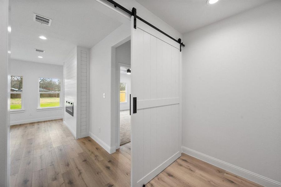 Hallway with baseboards, a barn door, visible vents, and wood finished floors