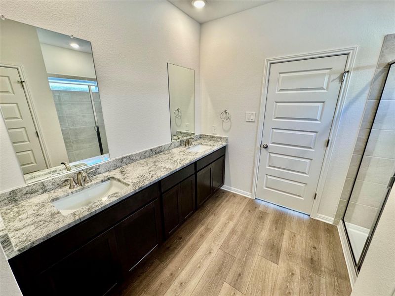 Bathroom with a stall shower, double vanity, light wood finished floors, and a textured wall