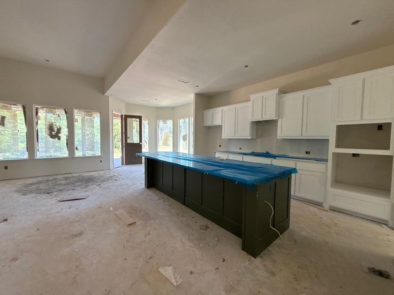 Spacious kitchen featuring a large central island, white cabinetry, integrated shelving, and abundant natural light from multiple windows