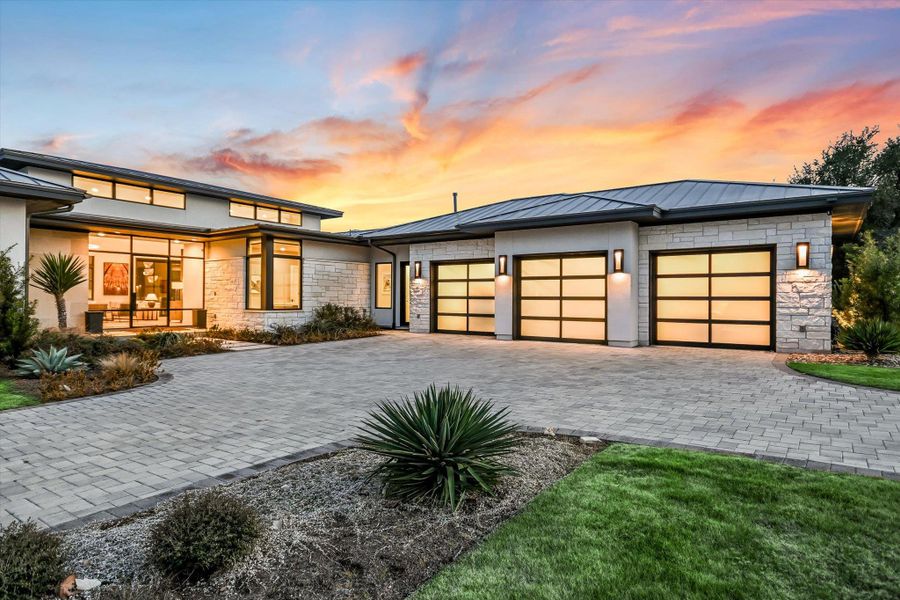 View of front facade featuring stone siding, a standing seam roof, an attached garage, and driveway View of front facade featuring stone siding, a standing seam roof, an attached garage, and driveway