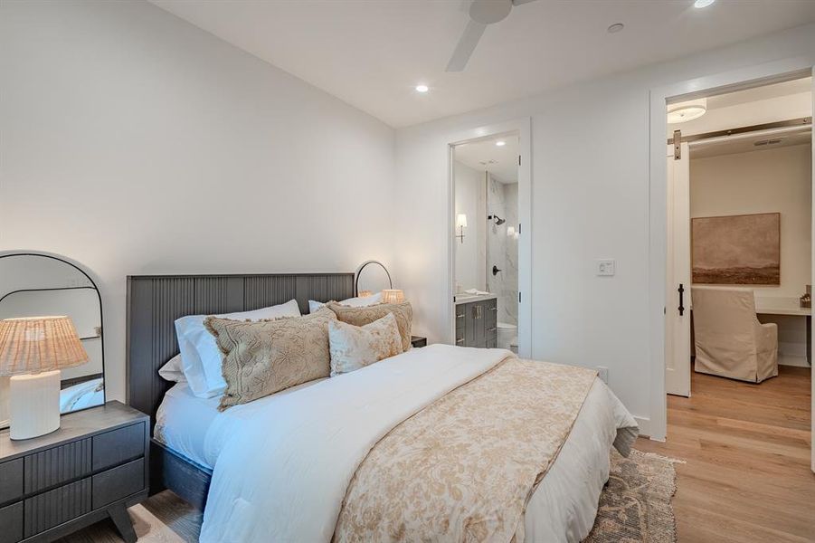 Bedroom featuring a barn door, light wood-type flooring, ensuite bathroom, ceiling fan, and recessed lighting Bedroom featuring a barn door, light wood-type flooring, ensuite bathroom, ceiling fan, and recessed lighting