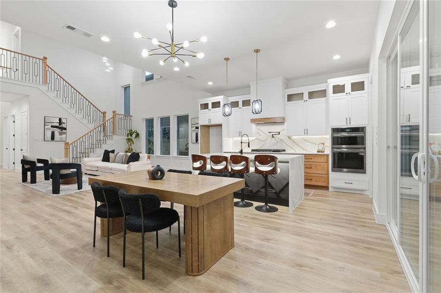 Two tone kitchen featuring a kitchen breakfast bar, glass fronted cabinets, a center island with sink, stainless steel double oven, and a chandelier