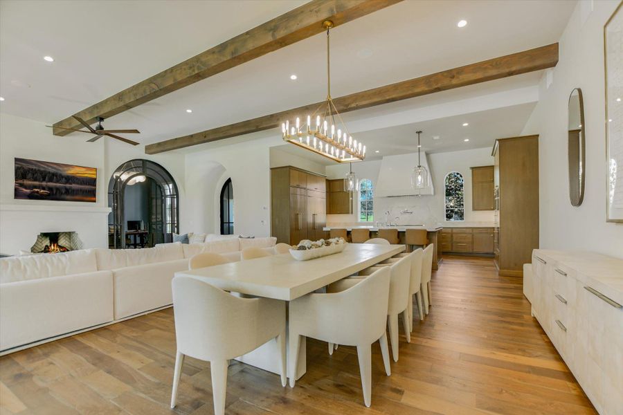 Dining space with beam ceiling, arched walkways, light wood finished floors, ceiling fan, and hanging lights