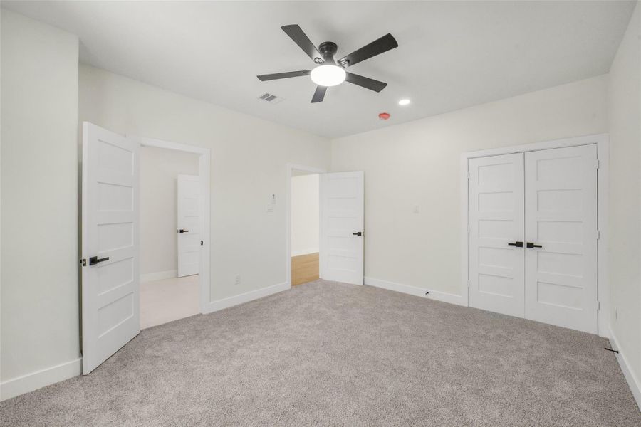 This photo shows a spacious room with soft carpeting, neutral walls, and a ceiling fan. It features multiple doors, likely leading to a closet and adjoining rooms, offering functional flow and ample storage.