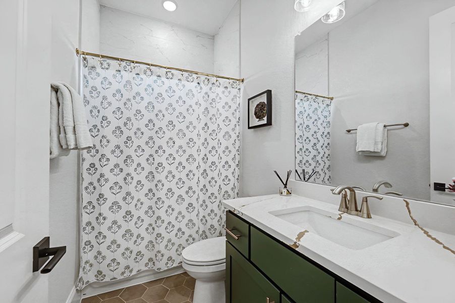 Secondary full bath with quartz countertop, green vanity, and shower/tub combo. Clean finishes and functional layout.