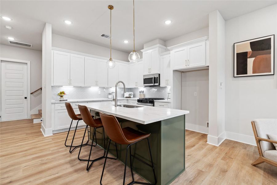 A refined kitchen anchored by a rosemary green accent island, layered with brass hardware and pendant lighting. Herringbone tile, under mount lighting, and soft close cabinetry complete the space with both warmth and precision.