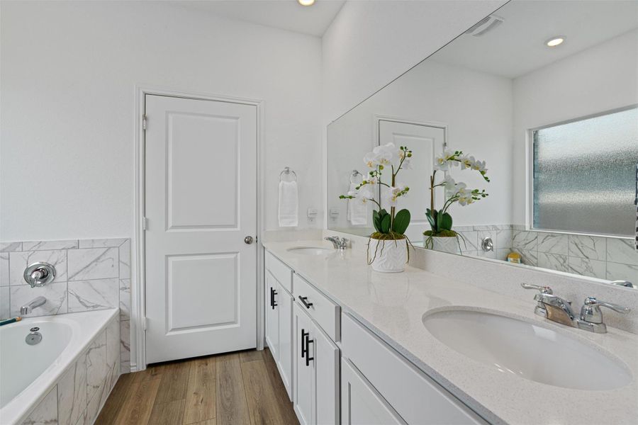 Bathroom featuring double vanity, wood finished floors, a bath, recessed lighting, and tile walls