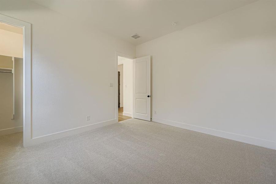 Unfurnished bedroom featuring light carpet and a spacious closet Unfurnished bedroom featuring light carpet and a spacious closet