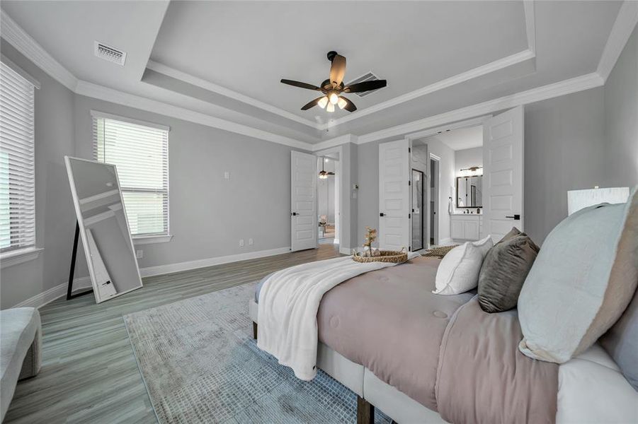 Bedroom with a tray ceiling, ornamental molding, ensuite bath, wood finished floors, and a ceiling fan Bedroom with a tray ceiling, ornamental molding, ensuite bath, wood finished floors, and a ceiling fan