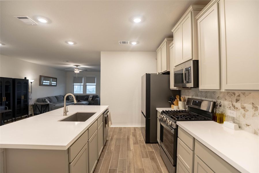 Kitchen with stainless steel appliances, open floor plan, wood finish floors, an island with sink, and gray cabinetry Kitchen with stainless steel appliances, open floor plan, wood finish floors, an island with sink, and gray cabinetry