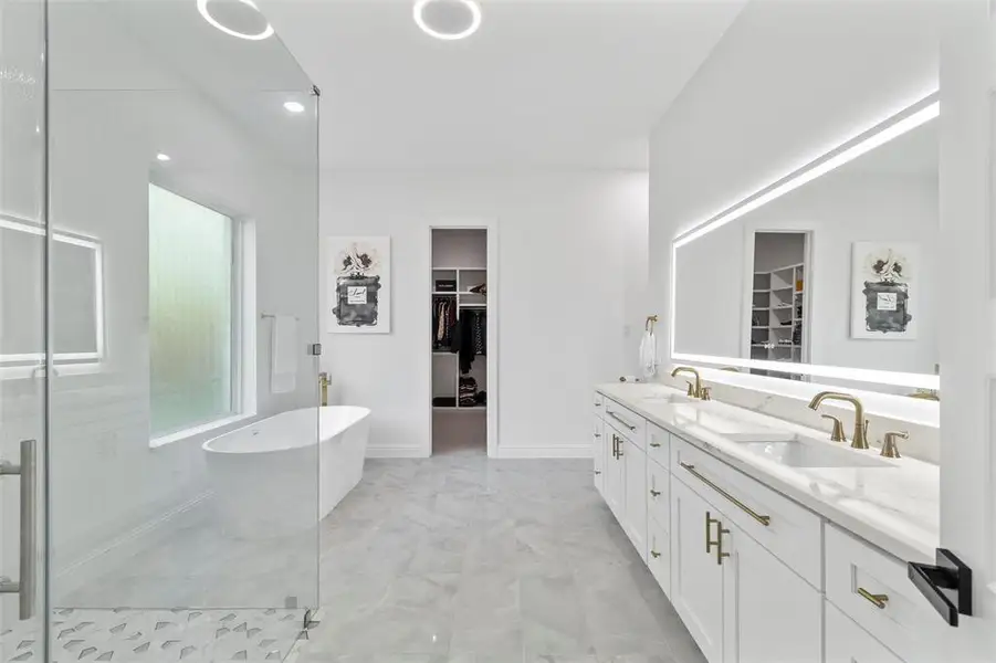 Modern bathroom with a freestanding soaking tub, a spacious glass-enclosed shower featuring patterned floor tiles, and a dual vanity with undermount sinks and gold-finish fixtures