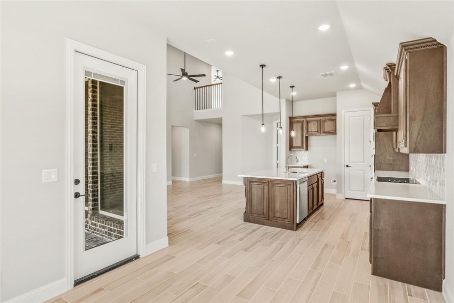 Open kitchen with dark wood cabinets, center island, pendant lights, and light wood-look tile floors opening to living area Open kitchen with dark wood cabinets, center island, pendant lights, and light wood-look tile floors opening to living area