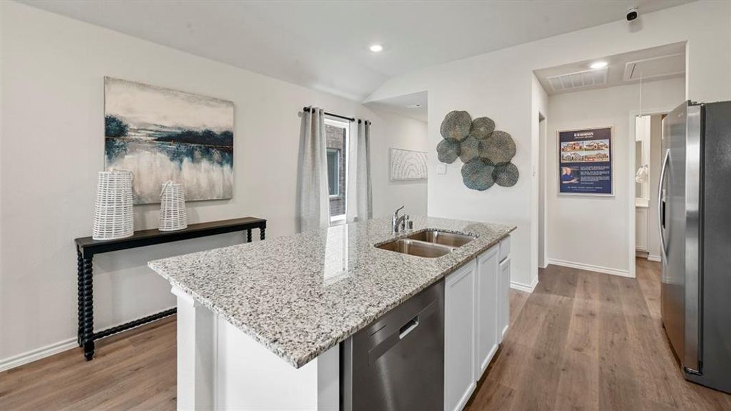 Kitchen with stainless steel appliances, light stone counters, light wood-type flooring, an island with sink, and white cabinetry Kitchen with stainless steel appliances, light stone counters, light wood-type flooring, an island with sink, and white cabinetry