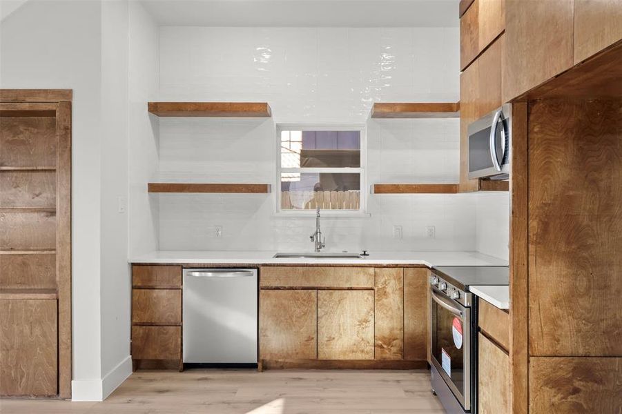 Kitchen with decorative backsplash, sink, stainless steel appliances, and light wood-type flooring