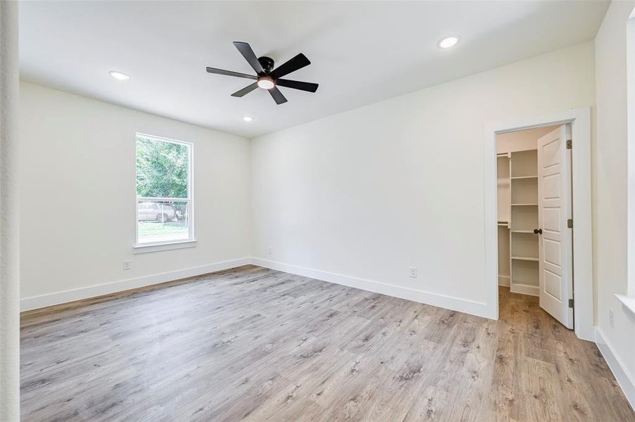 Spacious room featuring wood-finish flooring, a contemporary black ceiling fan with integrated lighting, recessed ceiling lights, and a window with white trim Spacious room featuring wood-finish flooring, a contemporary black ceiling fan with integrated lighting, recessed ceiling lights, and a window with white trim