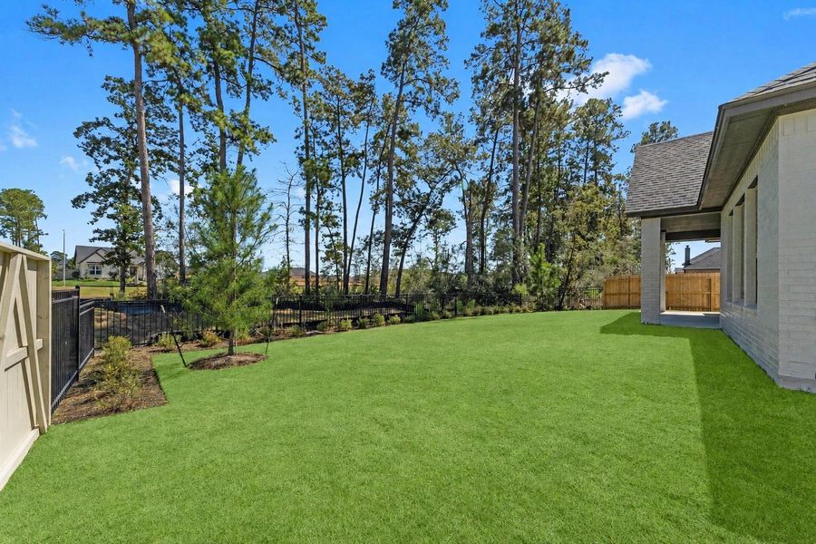 Backyard with lush landscaping, a wrought iron fence, and mature trees behind the property. Backyard with lush landscaping, a wrought iron fence, and mature trees behind the property.