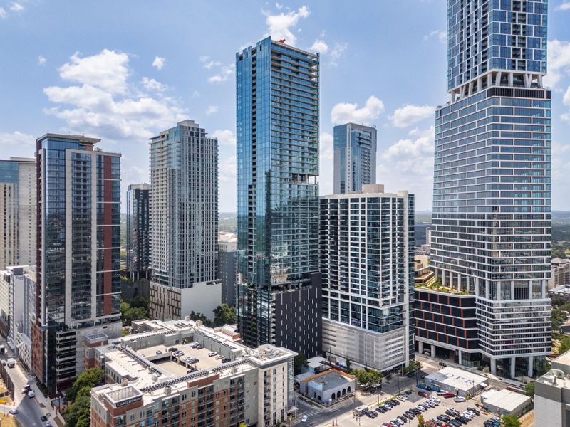An aerial perspective reveals a vibrant city skyline under a bright sky, showcasing a blend of high-rise structures and urban development.